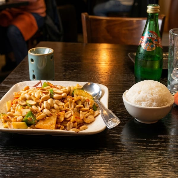 Kung Pao chicken with peanuts, rice, and a Perrier bottle on a dark wooden table.