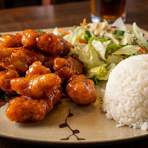 Sweet and sour chicken with white rice and a side salad on a decorative plate.