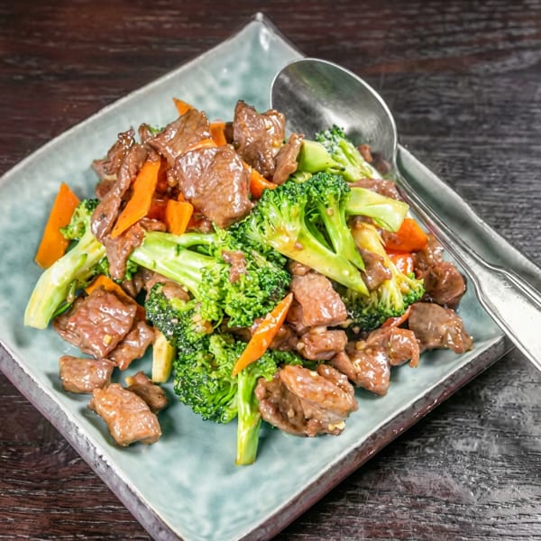 Beef and broccoli stir-fry with carrots on a light blue rectangular plate with a spoon.