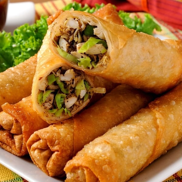 Crispy golden spring rolls, one cut open to show a savory chicken and vegetable filling, served with dipping sauce.