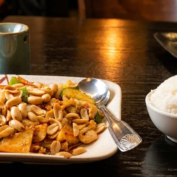 Kung Pao chicken with peanuts, bell peppers, and rice on a dark wooden table.