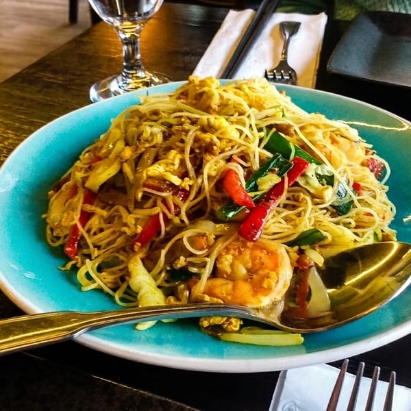 A vibrant plate of shrimp pad thai with noodles, vegetables, and egg on a dark wooden table.