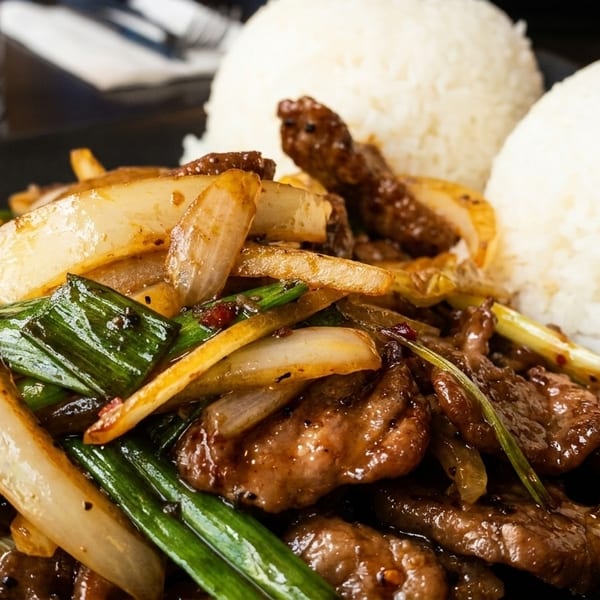 Stir-fried beef with onions and green scallions, served with two mounds of white rice.
