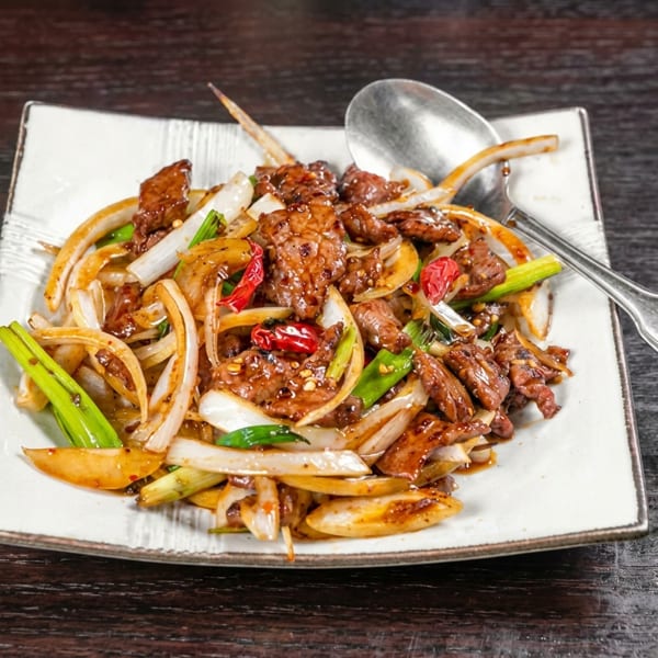 Stir-fried beef with sliced onions, green onions, and red chilies on a white plate.